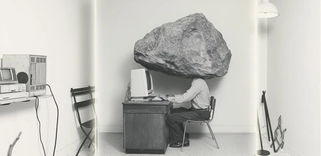 Burnout assessment service illustration representing a person sitting at a desk with a massive boulder balancing directly on their head