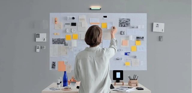 Job crafting wellbeing assessment illustration representing a person standing in front of a large wall-mounted mood board placing sticky notes and cards