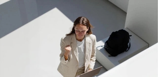 Job satisfaction wellbeing assessment illustration representing a high-angle view of a woman in a blazer celebrating with a clenched fist while holding a tablet