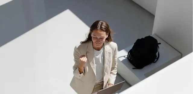 Job satisfaction wellbeing assessment illustration representing a high-angle view of a woman in a blazer celebrating with a clenched fist while holding a tablet
