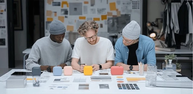 Team collaboration job skills service illustration representing three designers collaborating over small colourful smart speakers on a desk