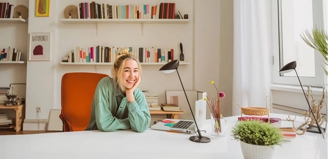 Work-life balance wellbeing assessment illustration representing a woman resting her chin on her hand and smiling while sitting at a bright, tidy home office desk